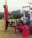Seen behind the tractor is the unit with stabilizers on the right and in the middle, and pile-driver on the left, ready to pound into the ground a 12-foot-high, big round wooden post.